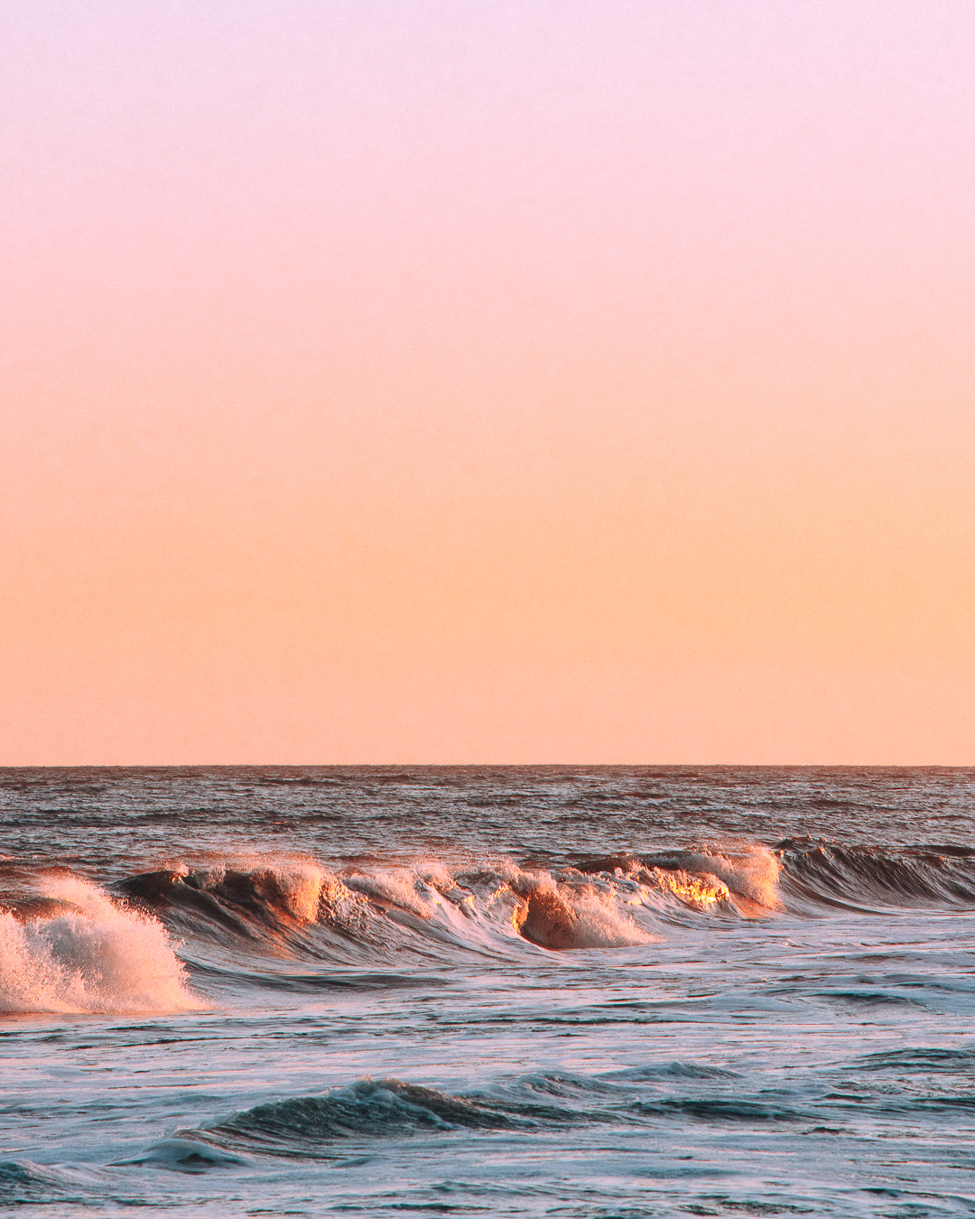 Waves gently crashing under a pastel pink and orange sunset sky.